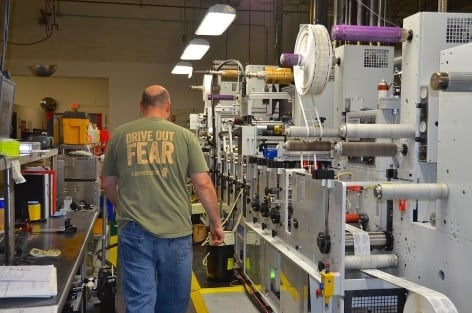 Employee in a tshirt with the text 'Drive out fear" next to label printing machines.