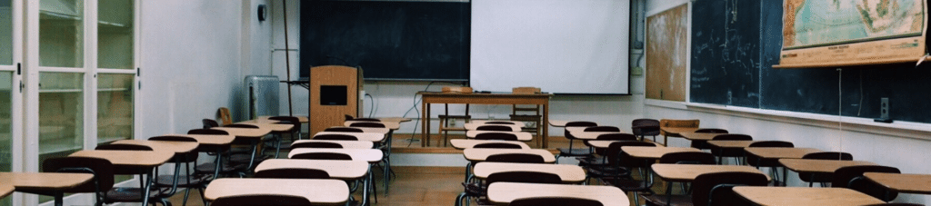 Empty classroom with desks facing a teacher's lectern, desk, and blackboard.