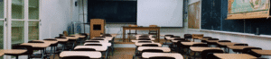 Empty classroom with desks facing a teacher's lectern, desk, and blackboard.