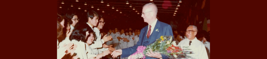 Dr. Deming holding a bouquet of flowers shaking hands with factory workers in Japan.
