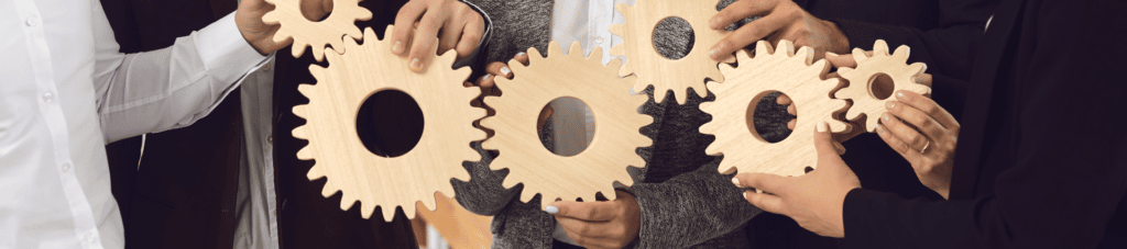 Series of wooden gears in a horizontal line, each held by a person's fingers.