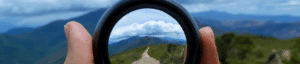 Looking through a lens that has a clear/crisp image of a dirt road leading into the distance, surrounded by a blurry image of the landscape photo beyond the lens.