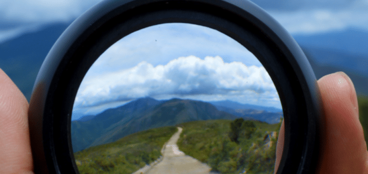 Looking through a lens that has a clear/crisp image of a dirt road leading into the distance, surrounded by a blurry image of the landscape photo beyond the lens.
